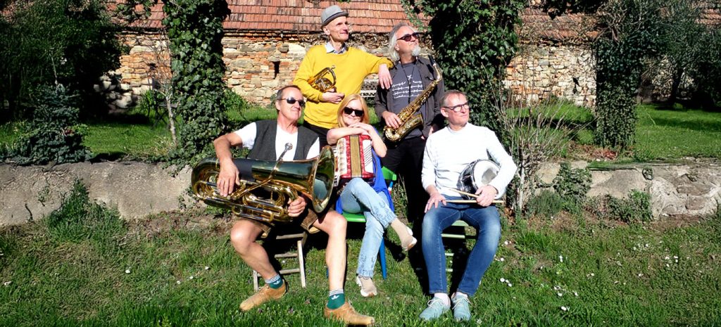 Portrait der Band Multikulti vo einem alten Bauernhaus und auf grünem Grass